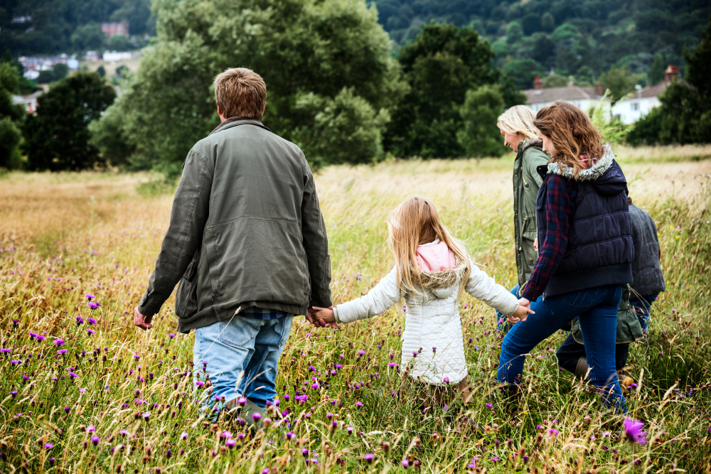 Mehrere Personen, darunter ein Kind, gehen Hand in Hand über eine blühende Wiese.