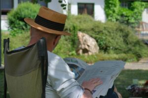 Person sitzt im Freien auf einem Stuhl und liest eine Zeitung.