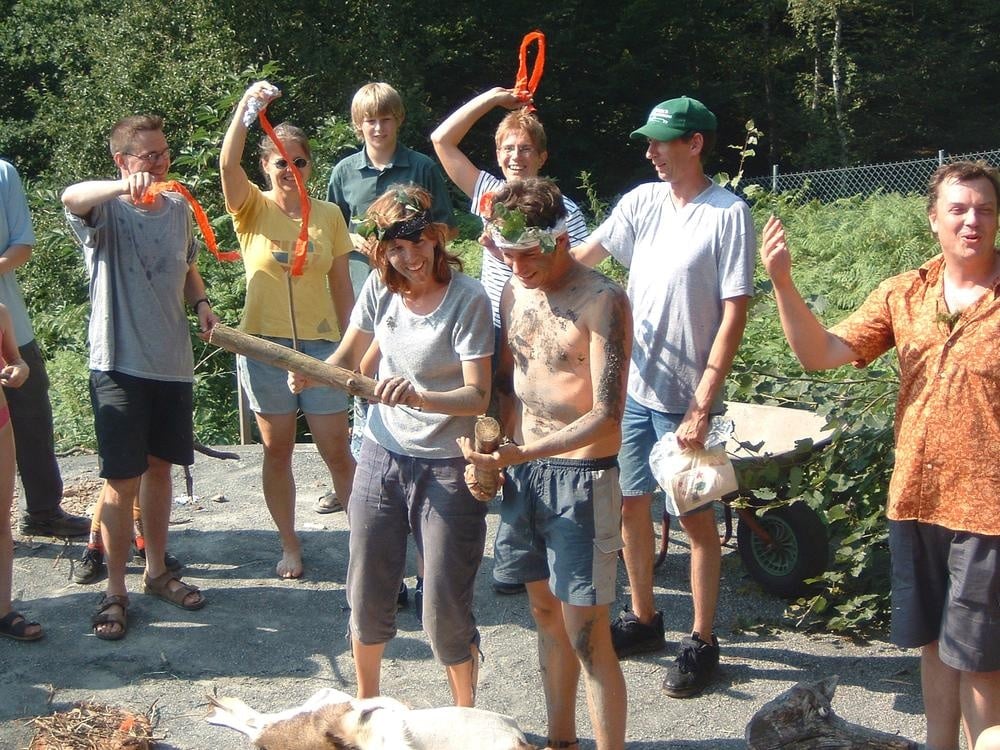 Gruppe von Erwachsenen steht im Freien zusammen, zwei Personen halten Gegenstände in den Händen, andere Personen heben Bänder oder schauen zu.