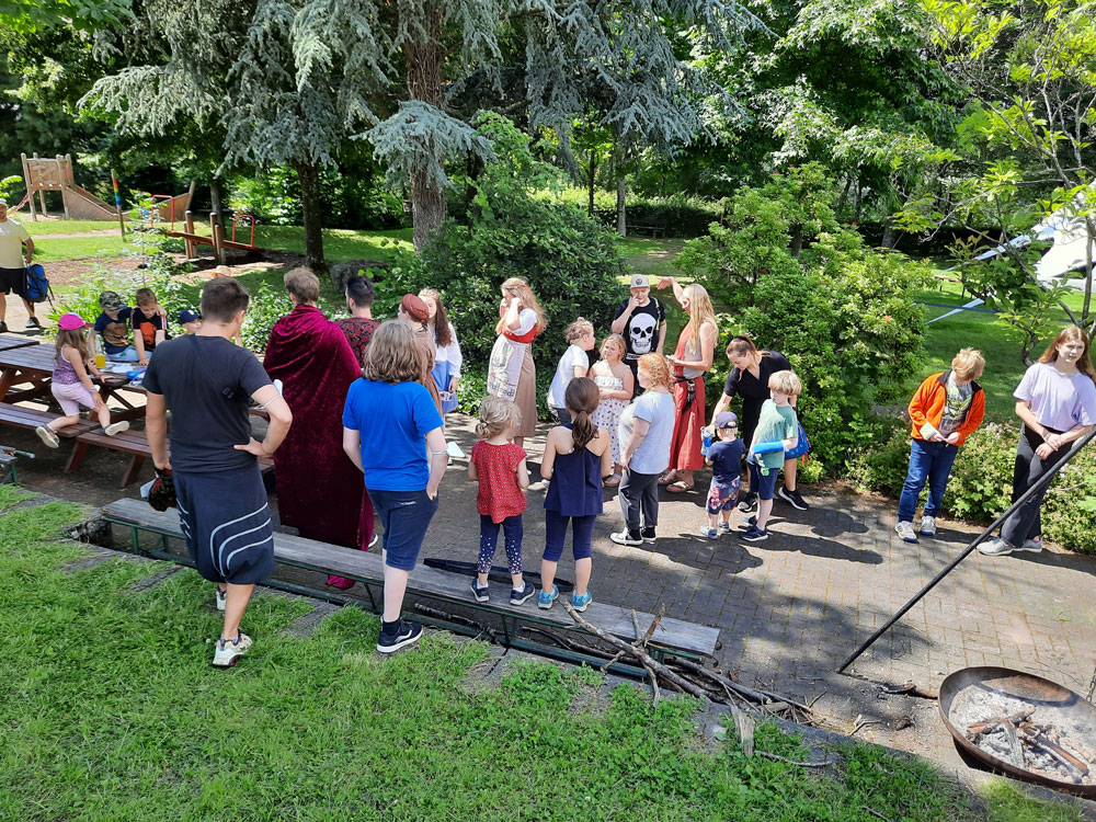 Gruppe von Kindern und Erwachsenen steht im Außenbereich eines Gartens oder Geländes zusammen.